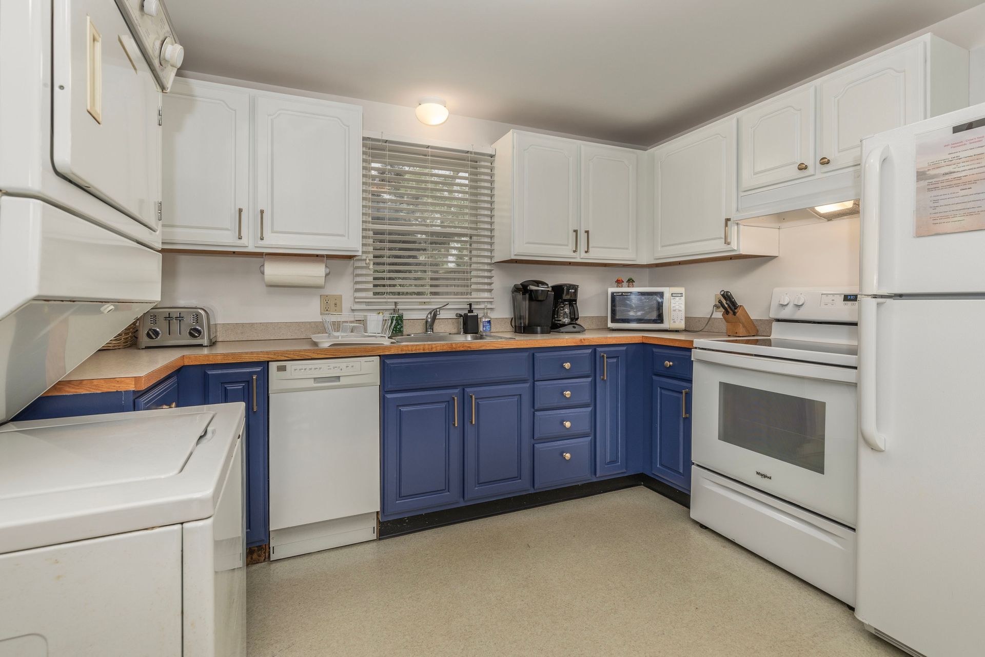 A kitchen with blue cabinets , white appliances , and a washer and dryer.