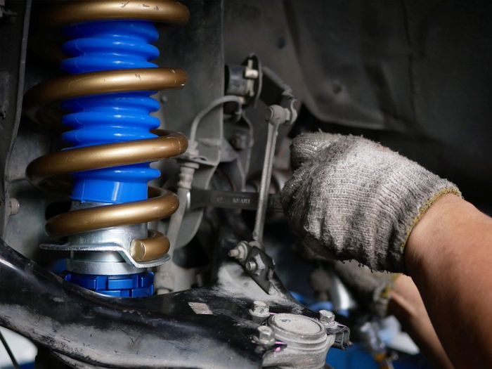 A gloved hand using a wrench to work on a car's suspension system | American Muffler & Auto Repair