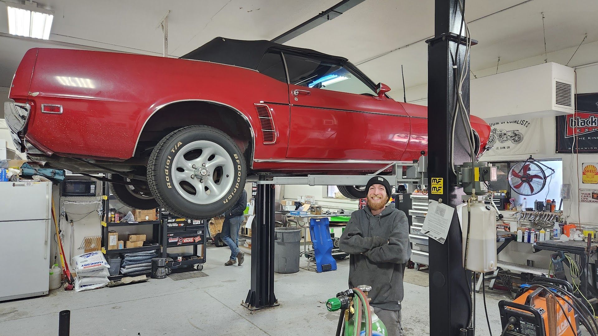 Man standing in a garage with a red convertible on a lift. | American Muffler & Auto Repair
