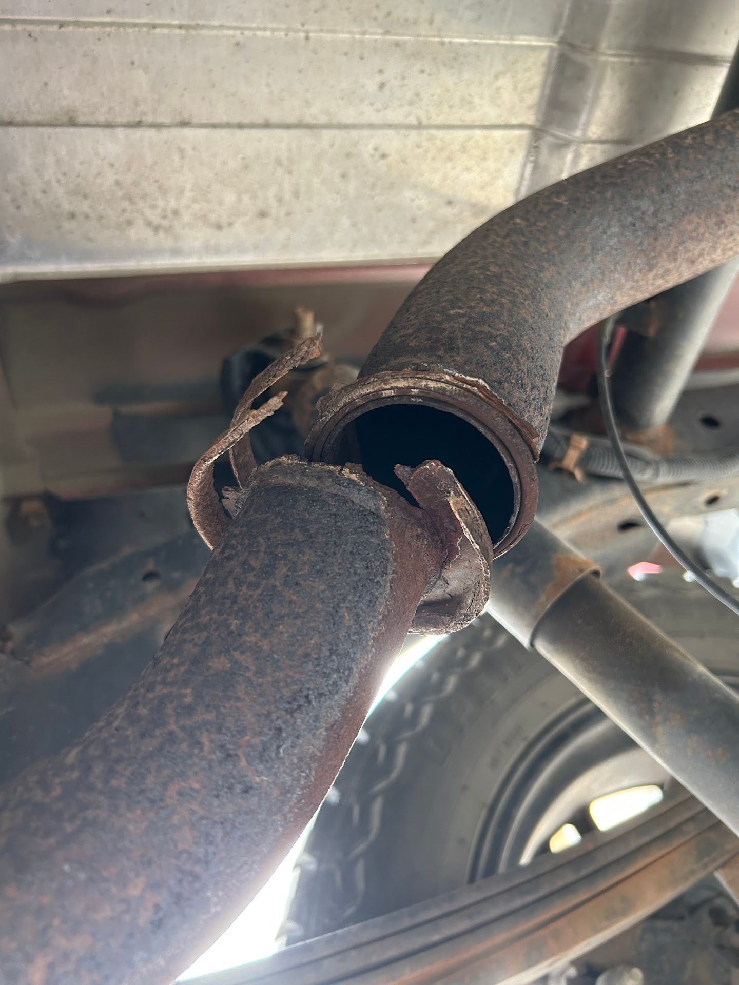 Rusty car exhaust pipe with a significant break. Located underneath a vehicle. | American Muffler & Auto Repair