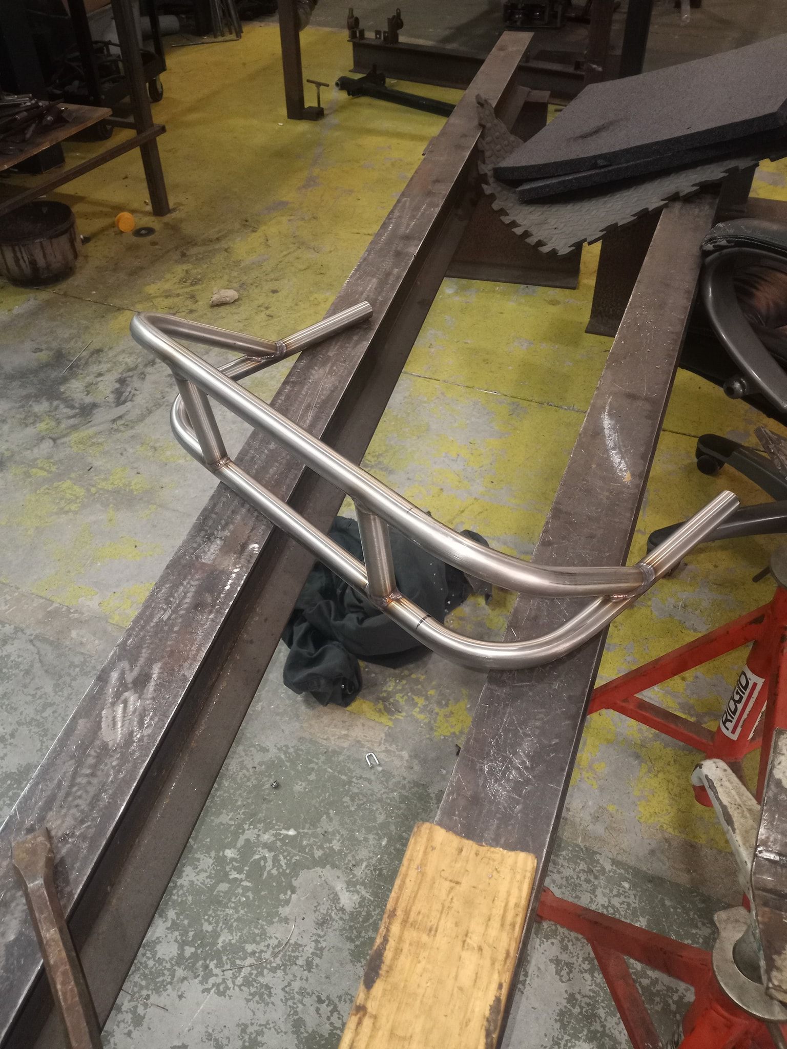 Metal tubing motorcycle frame on wood beams in a workshop.
