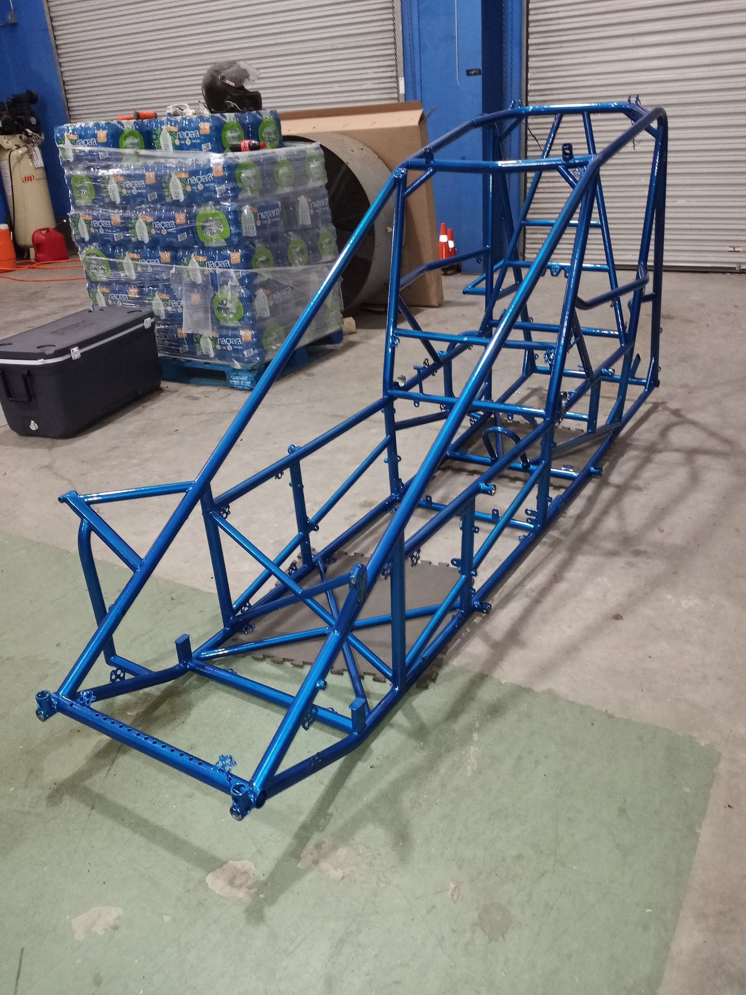 Interior view of a building under construction with exposed steel beams, concrete walls, and dirt floor.
