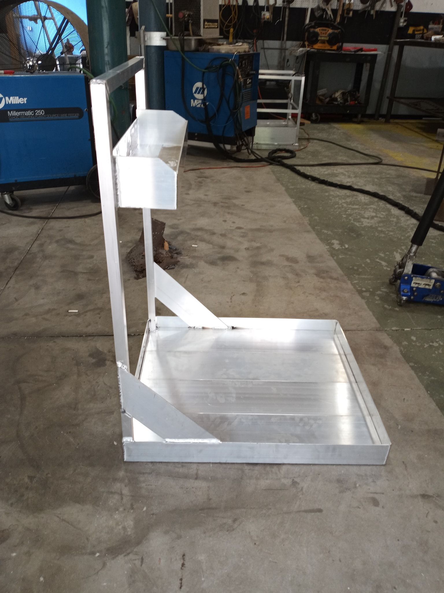 Metal cart in a workshop; it has a platform base, a storage area and a vertical back support.
