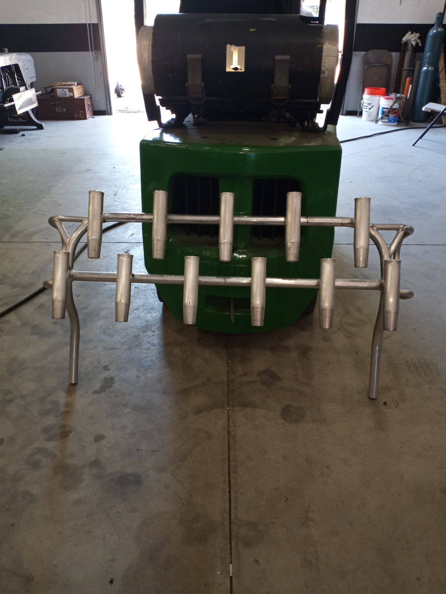 Metal stand with eight arms in front of a green industrial machine.