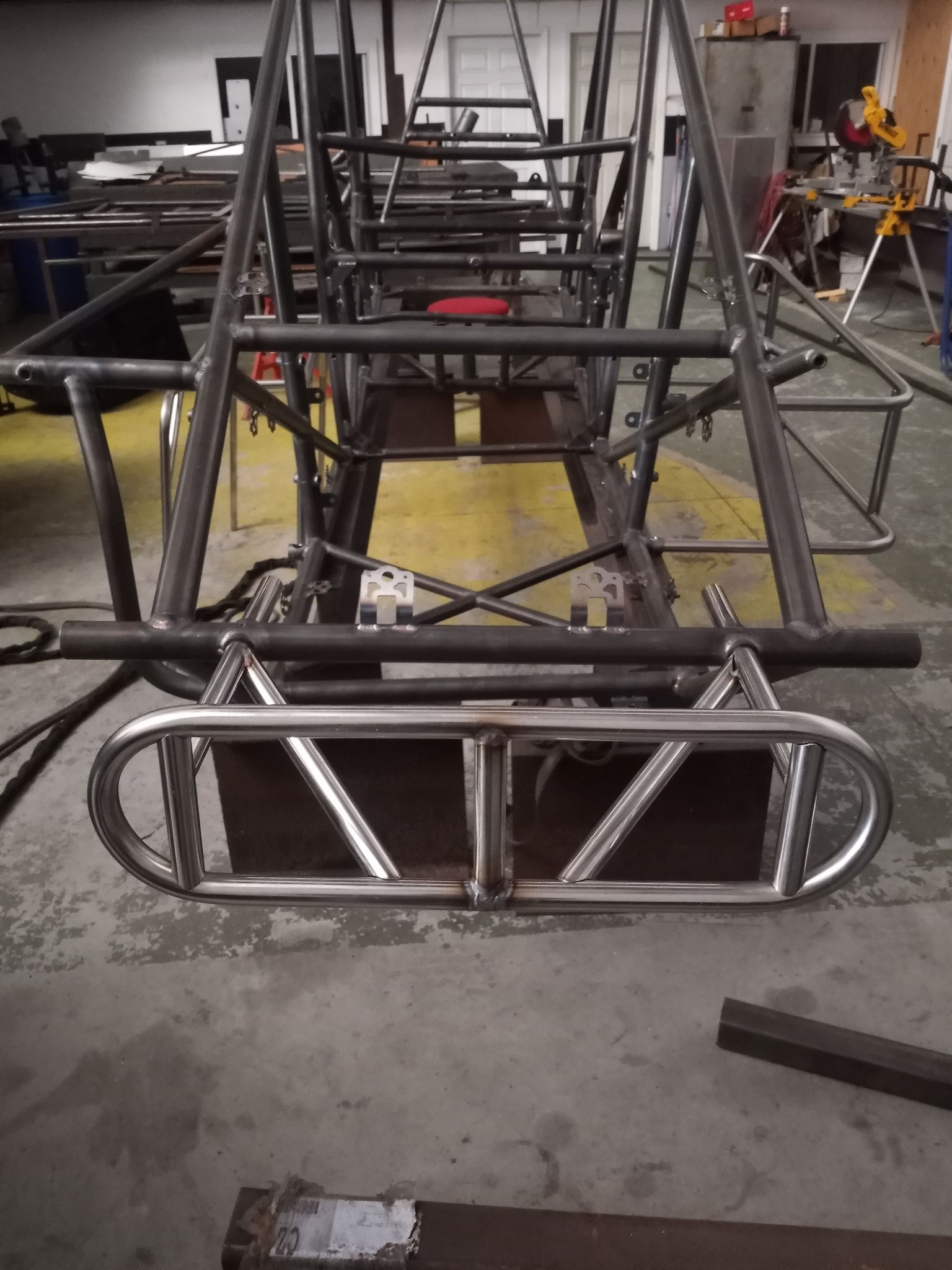 A metal roll cage frame, likely for a vehicle, sits on a workshop floor.