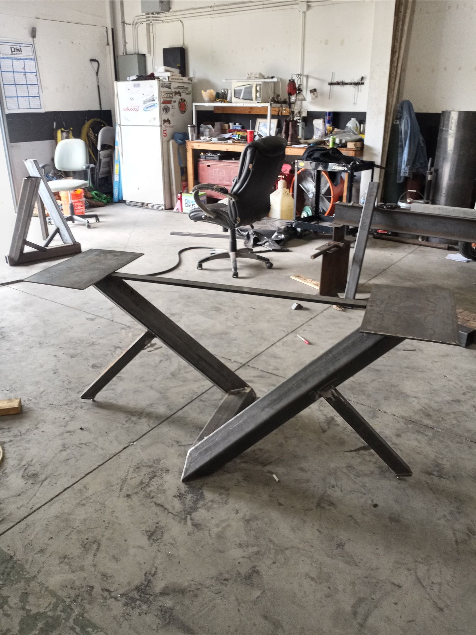 Two unfinished steel table legs in a workshop.