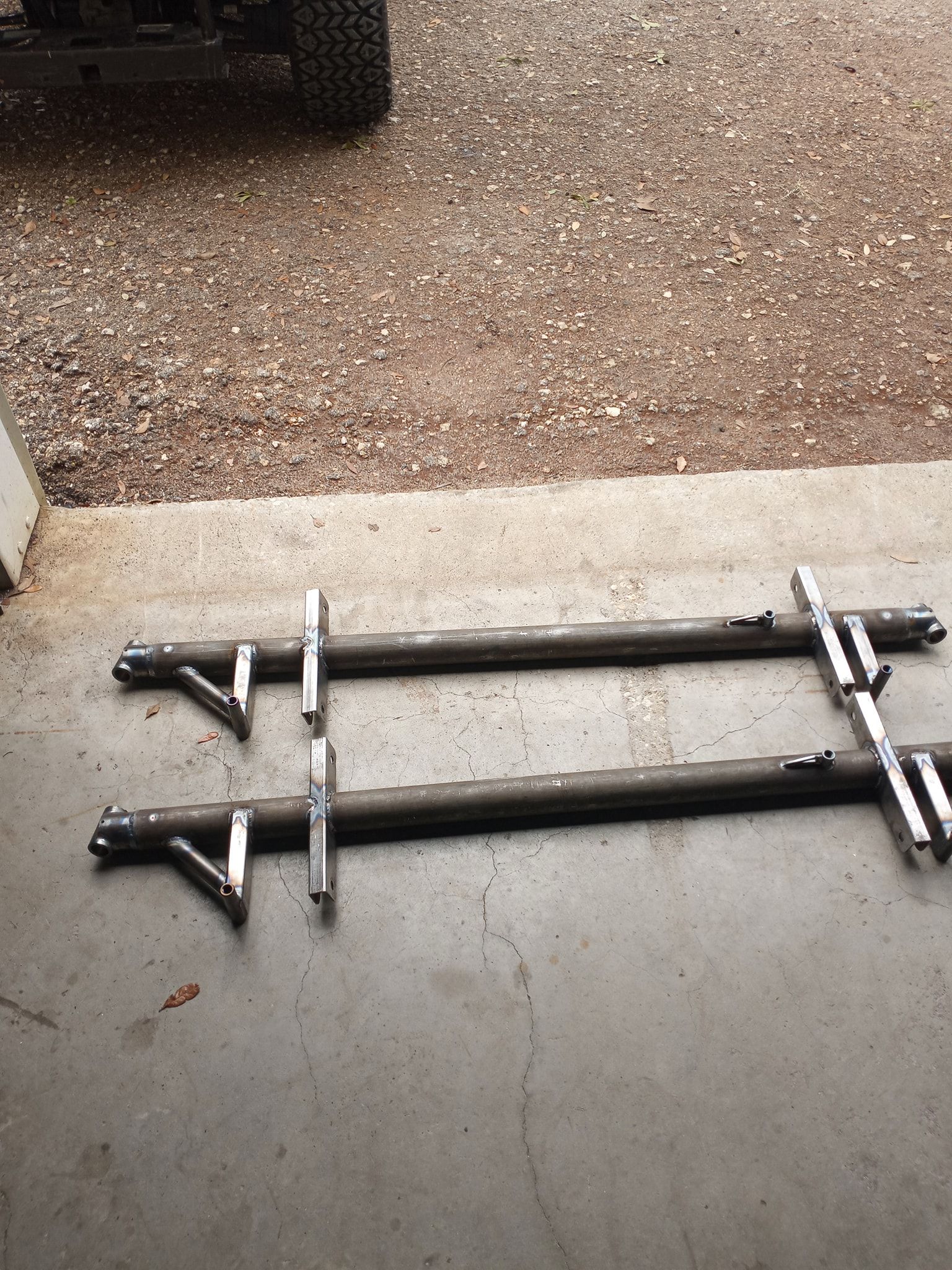 Two long, metal bars with welded brackets, lying on a concrete surface.