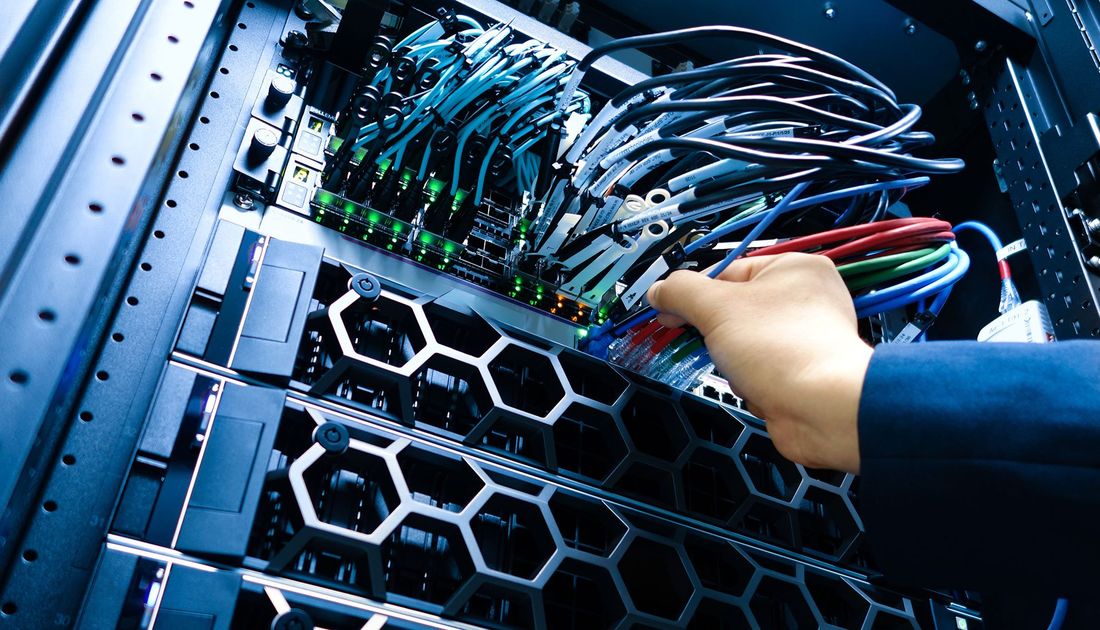 Hand connecting network cables in a server rack with blue and green cables.
