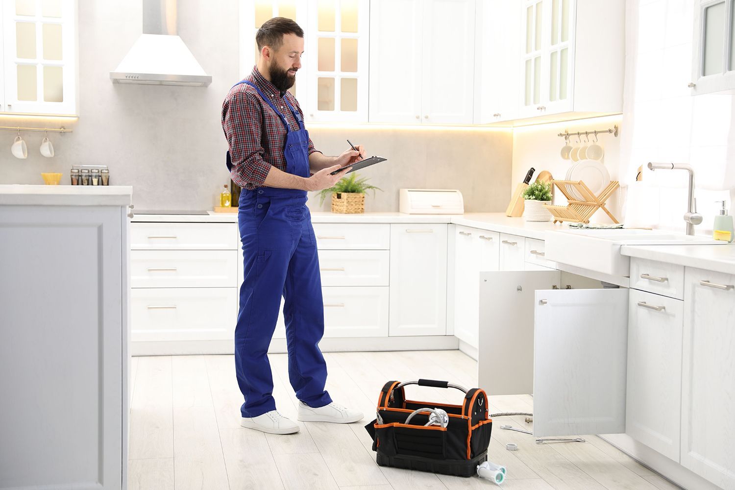 Residential plumbing contractor in uniform with clipboard writing in kitchen.
