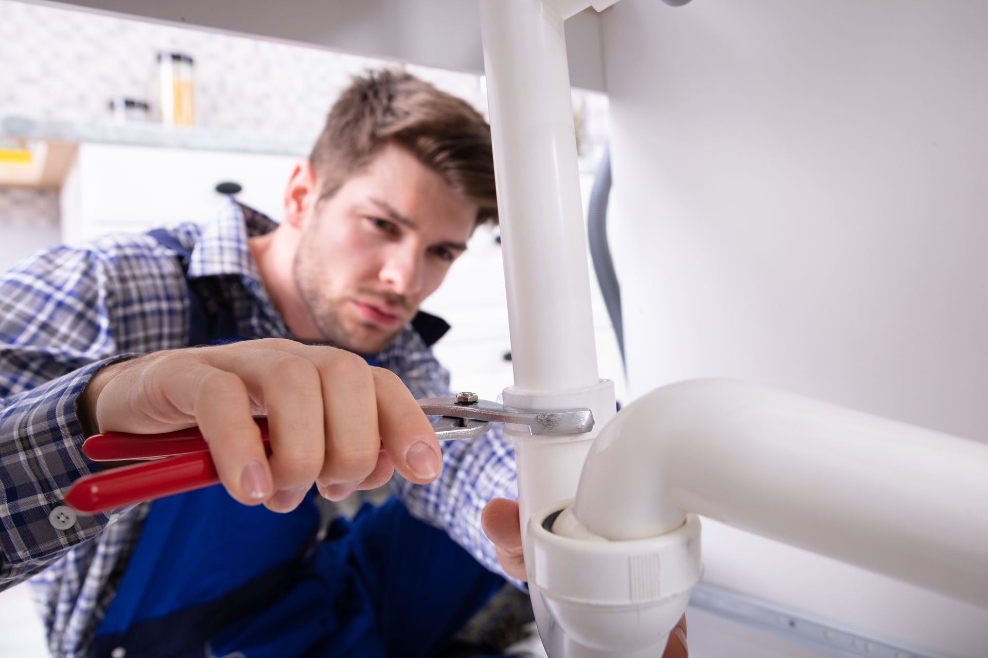 A plumber using a wrench on pipes while providing essential plumbing services in a kitchen.
