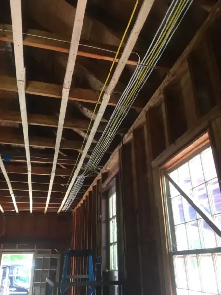 Electrical wiring running along the wooden ceiling of a building under construction, near a window.