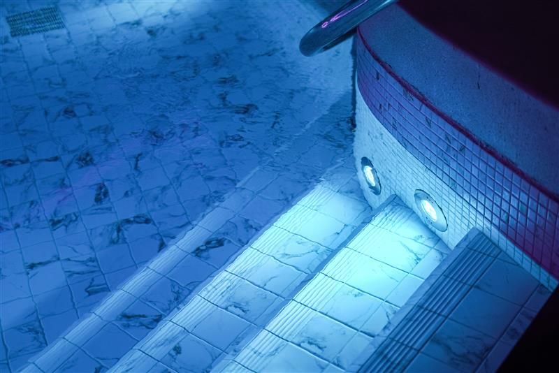 Blue-lit pool interior with tiled steps leading to the water. Two lights illuminate the edge.