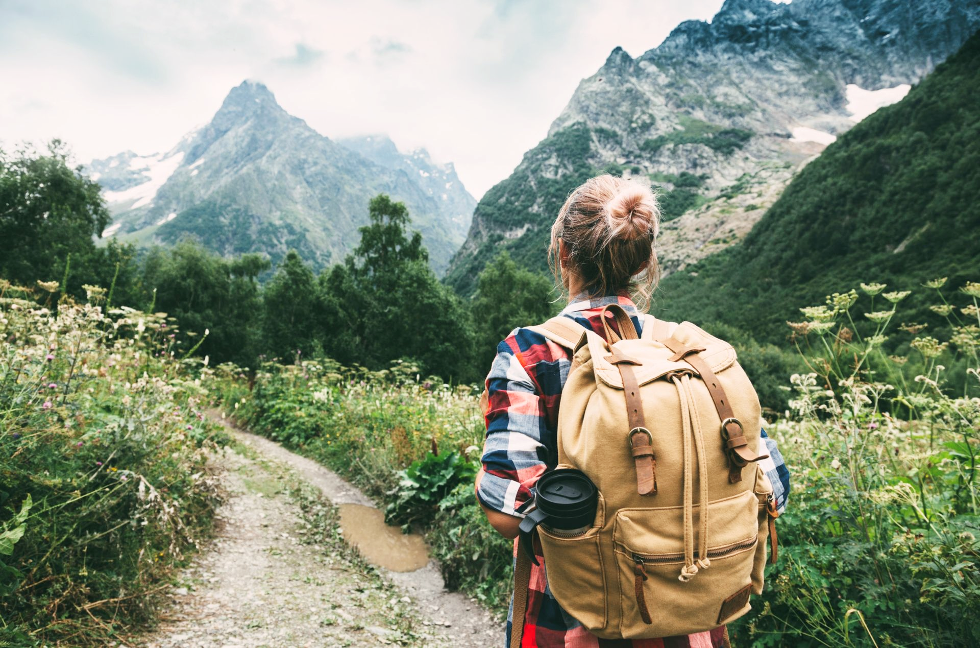 Woman with backpack hikes on a trail towards mountains.