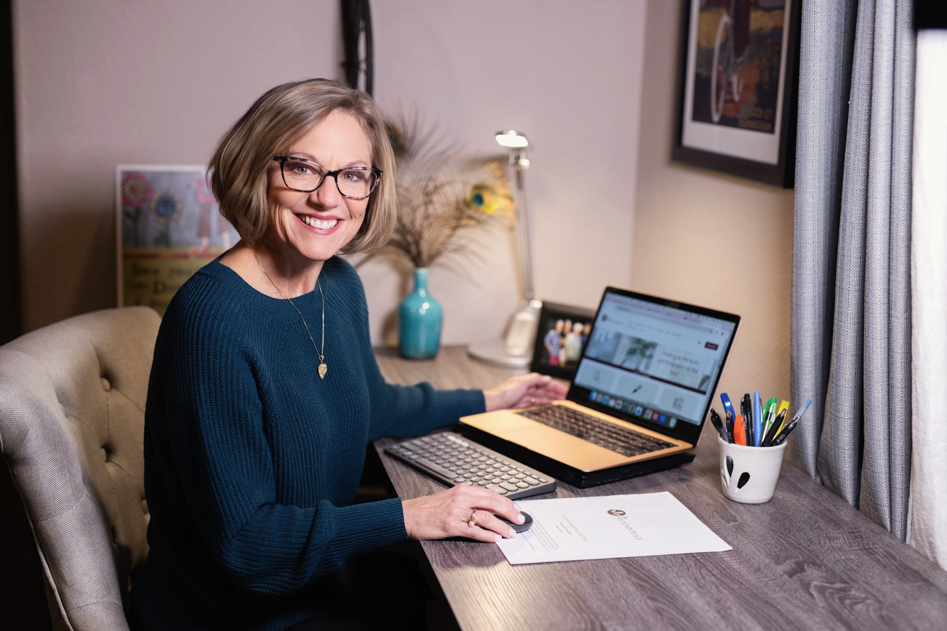 Joy Mitchell smiling at a desk, using a laptop, with a keyboard and mouse.