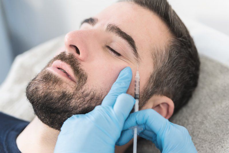 A man with a beard is getting a botox injection in his face.