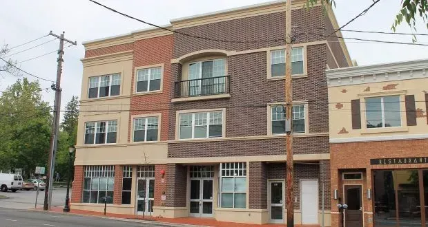 A large brick building with a balcony is sitting on the corner of a street.