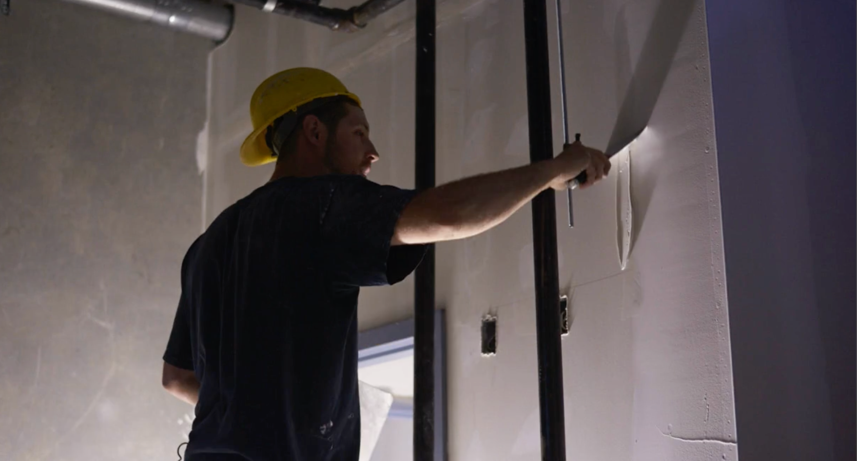 A man wearing a hard hat is plastering a wall.