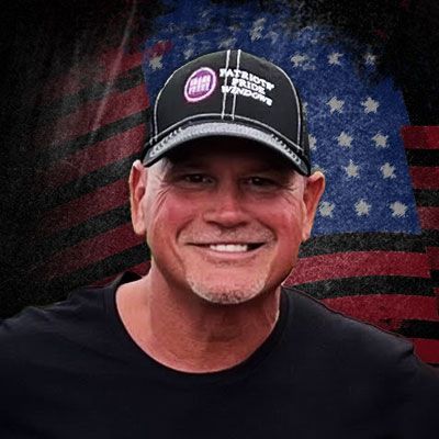 A man wearing a hat is smiling in front of an american flag.