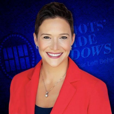 A woman in a red jacket is smiling in front of a blue background.