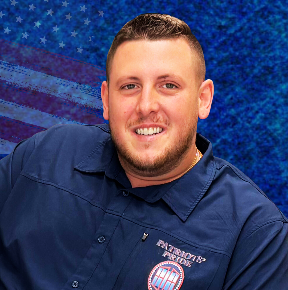 A man in a blue shirt is standing in front of an american flag.