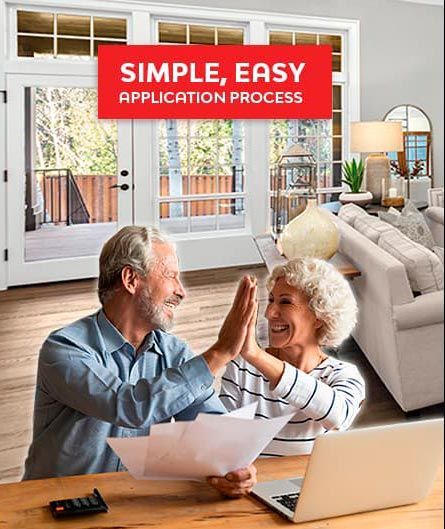 An older couple is giving each other a high five while sitting at a table with a laptop.