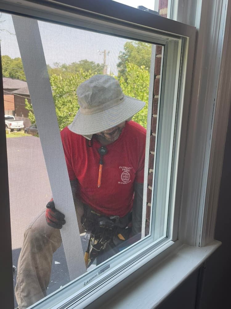 A man wearing a hat is working on a window.