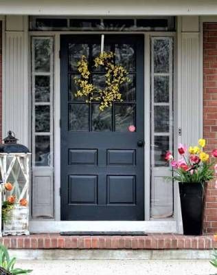 A black front door with a wreath hanging on it is on a brick house.