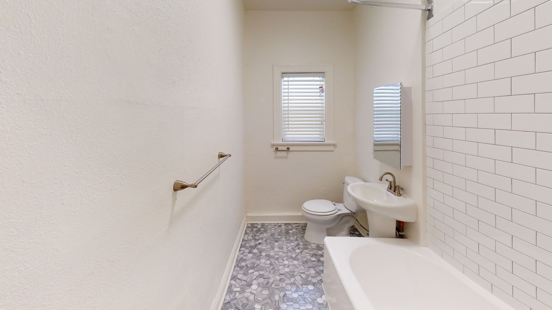 Small, white bathroom with mosaic tile floor, toilet, sink, tub, and window.