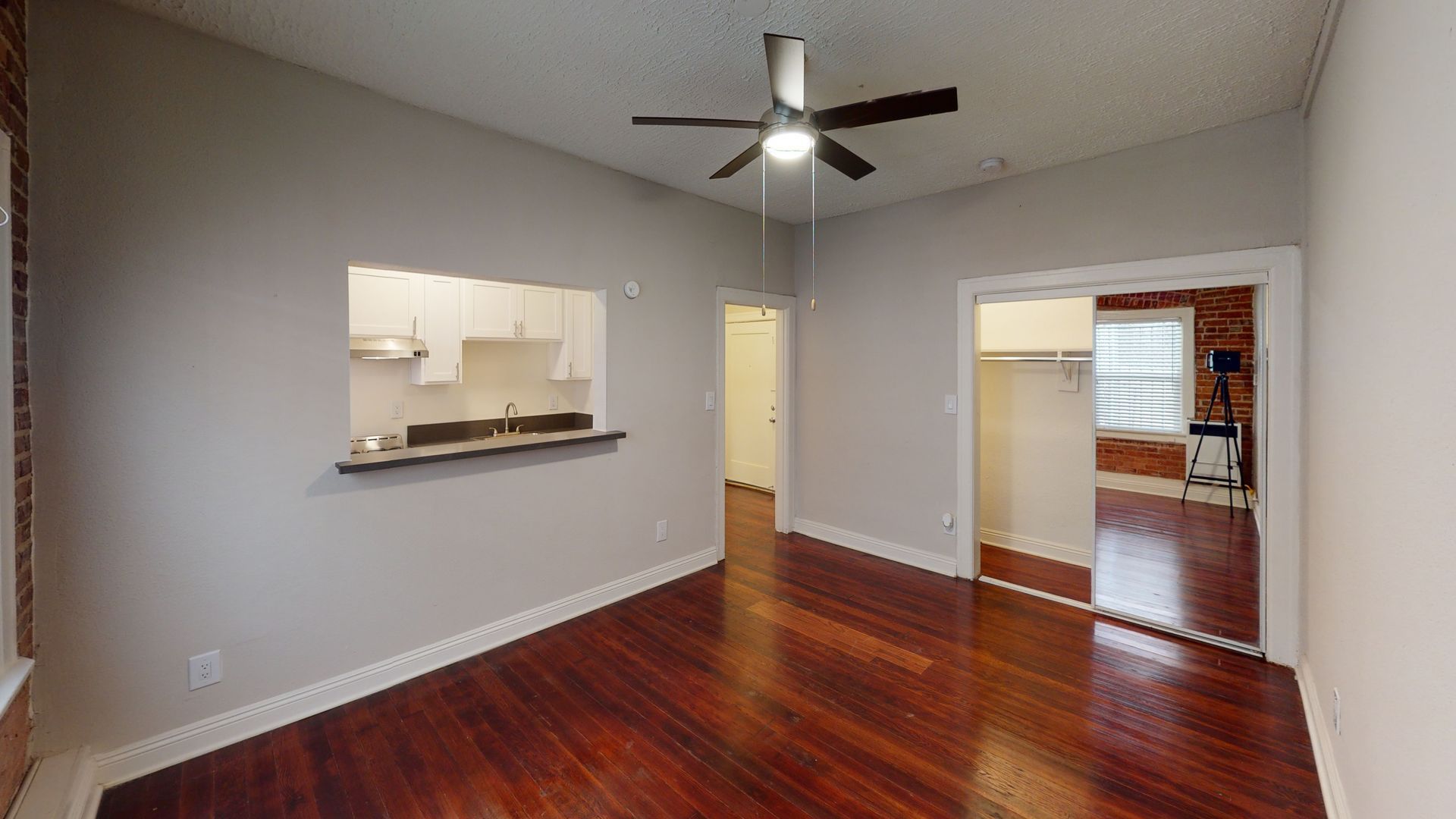 Empty living space with hardwood floors, a kitchen pass-through, and a ceiling fan.