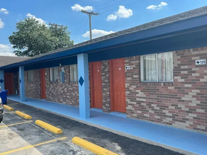 Motel exterior with blue trim, brick walls, and orange doors. Parking with yellow curbs.