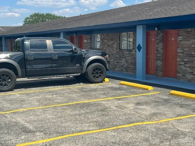 Black pickup truck parked in front of a motel with red doors and blue trim on a sunny day.
