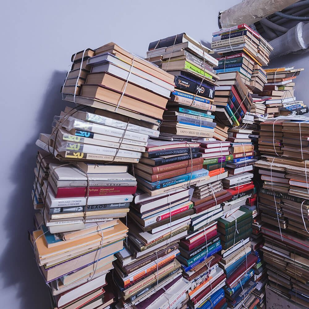 Piles of assorted books tied with rubber bands stacked against a wall.