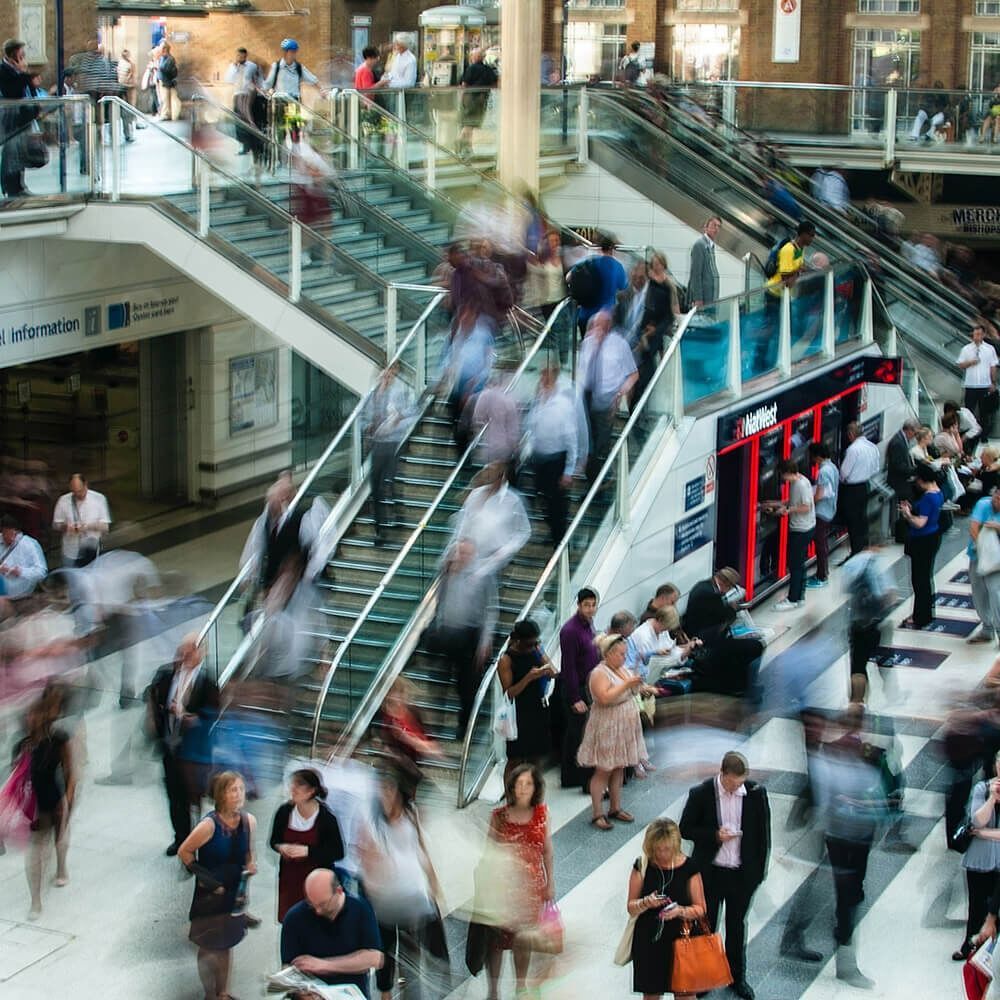 People blurred by movement in a busy train station, walking on escalators and stairs.