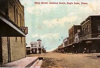 Main Street, Eagle Lake, Texas, looking south.  Buildings line a dusty street; a few people and a horse-drawn carriage are pr