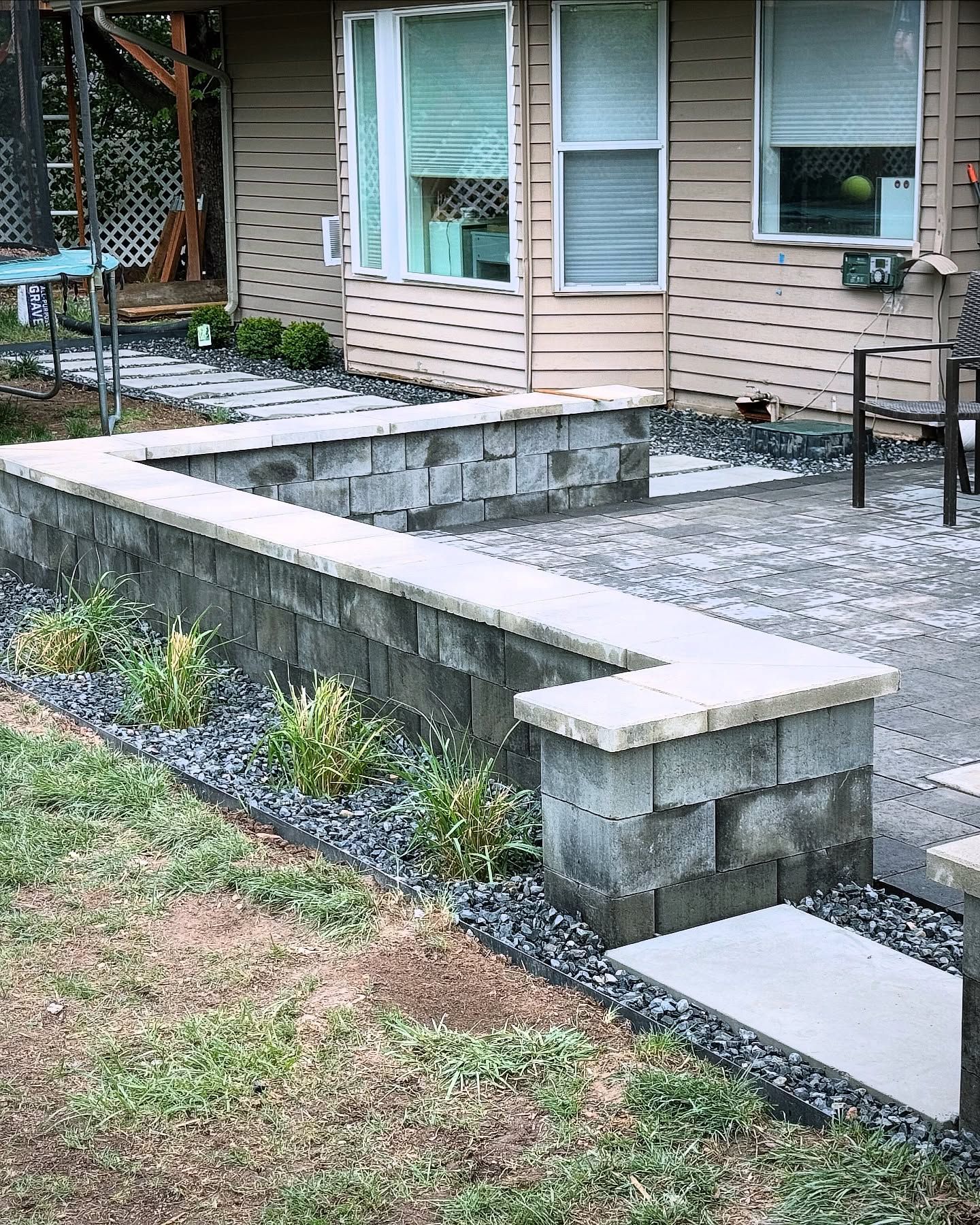 A zigzag-shaped retaining wall made of gray blocks with a light-colored top, separating a patio from a grassy lawn.