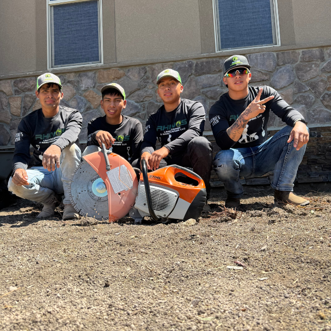 Four men in work attire pose with construction saws on a gravel surface in front of a building.