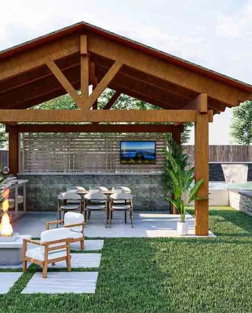 Wooden patio cover with outdoor kitchen, seating area, fireplace, and television in a backyard setting.