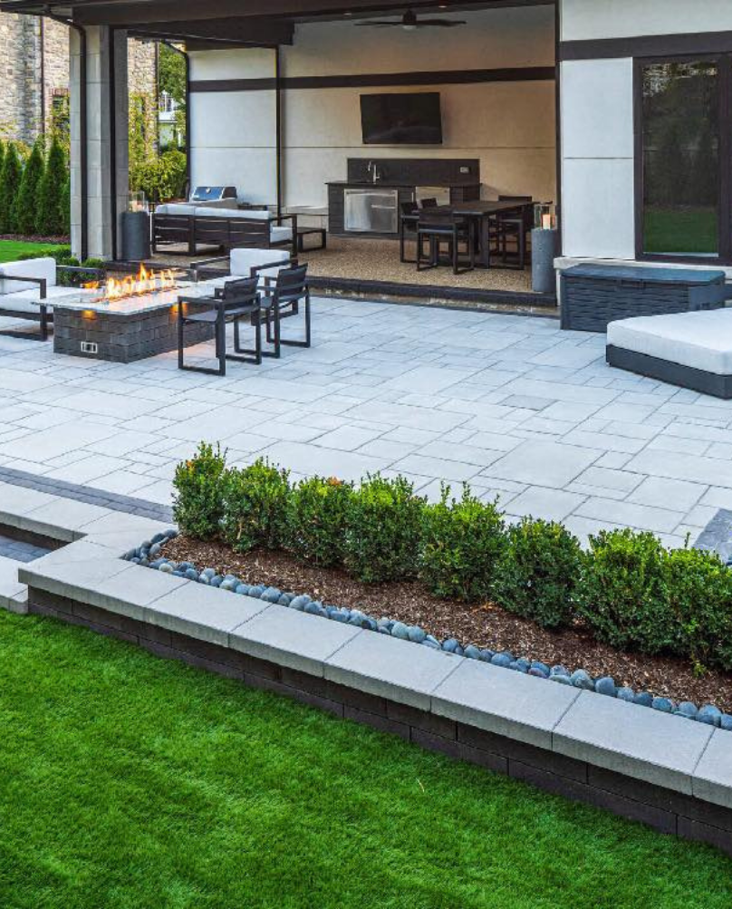 Outdoor patio with a fire pit, seating, and an outdoor kitchen. A modern design with a green lawn.