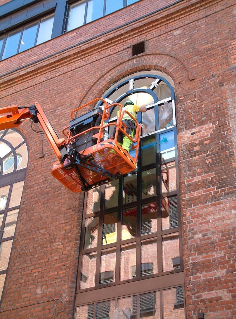 A man in a crane is cleaning a window on a brick building