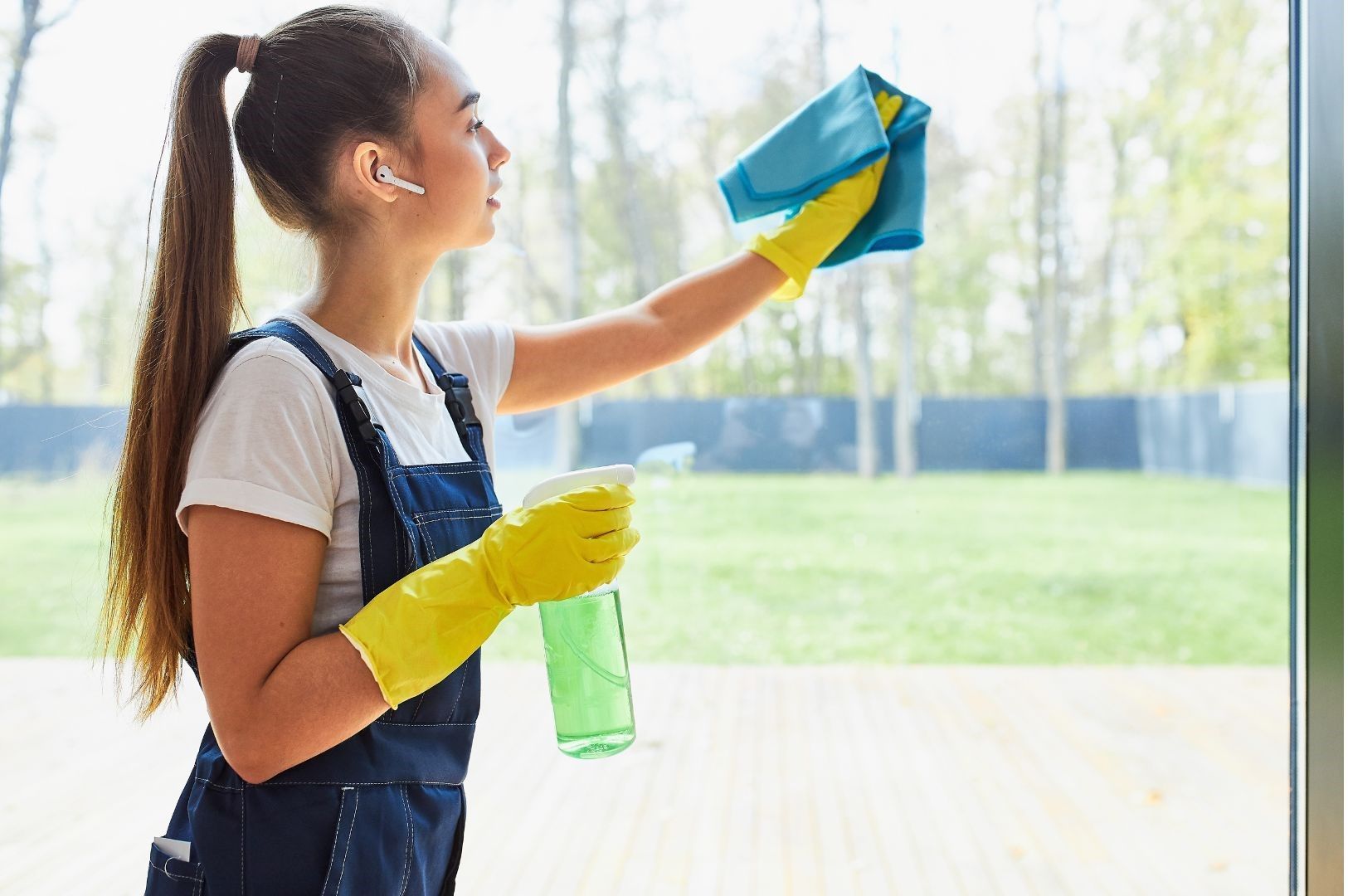 A woman is cleaning a window with a cloth and spray bottle.