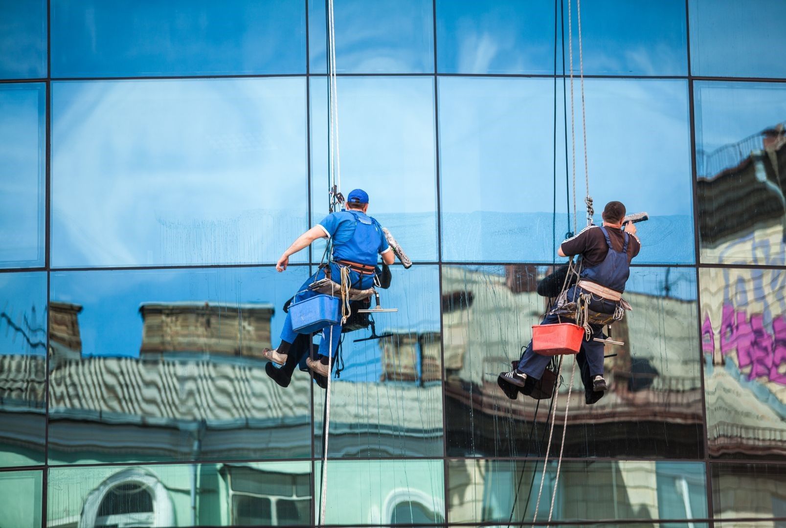 Two men are cleaning the windows of a tall building.