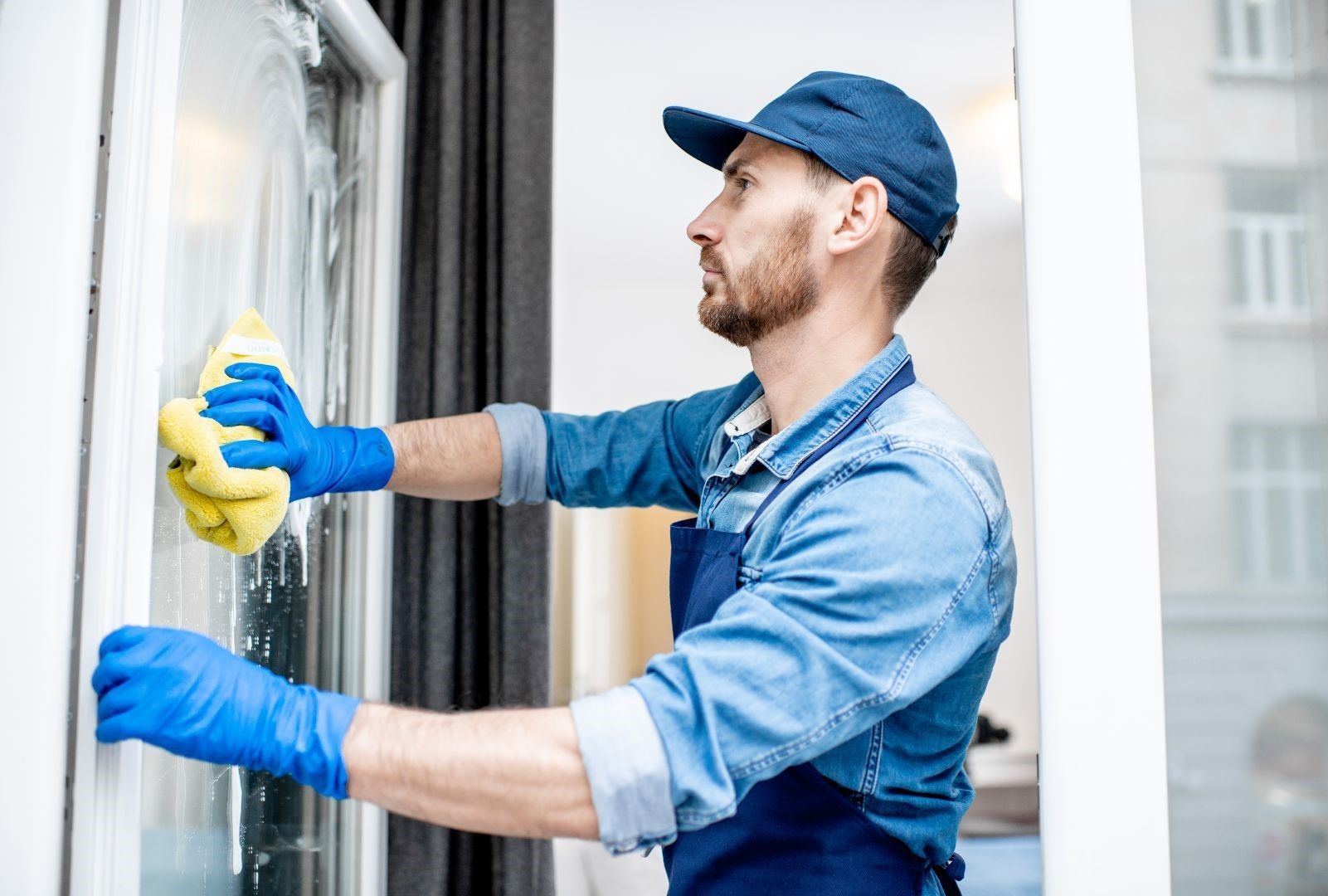A man is cleaning a window with a sponge and gloves.