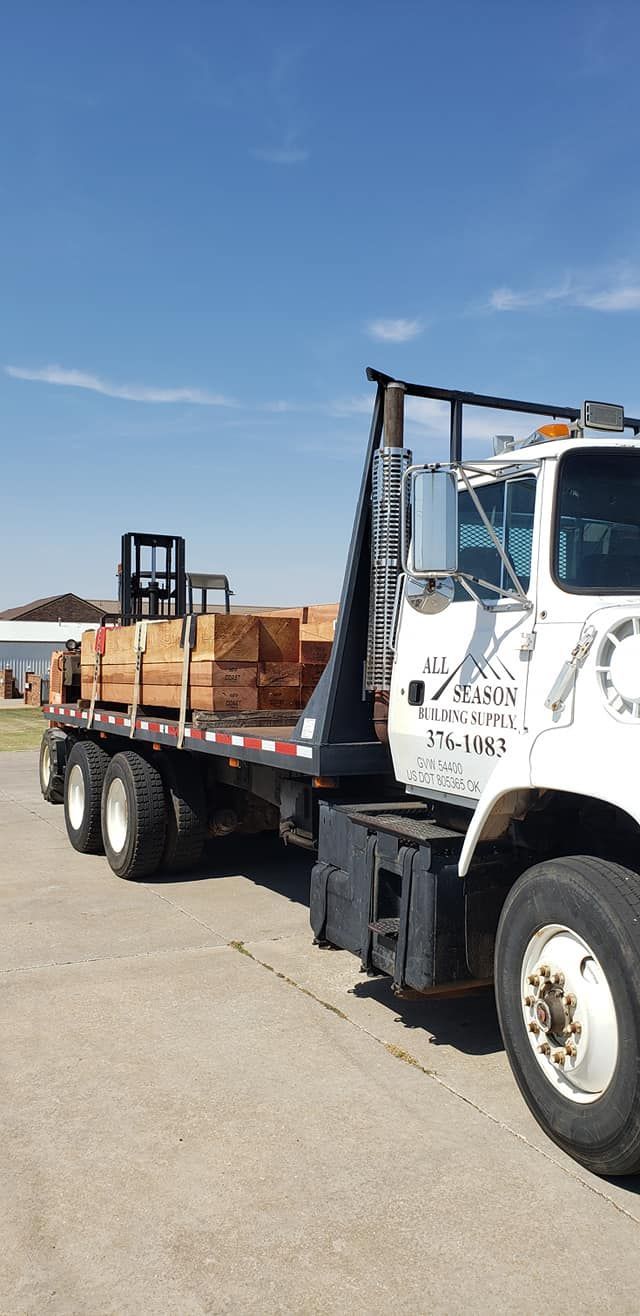 A flatbed truck loaded with lumber sits on a paved surface under a blue sky.