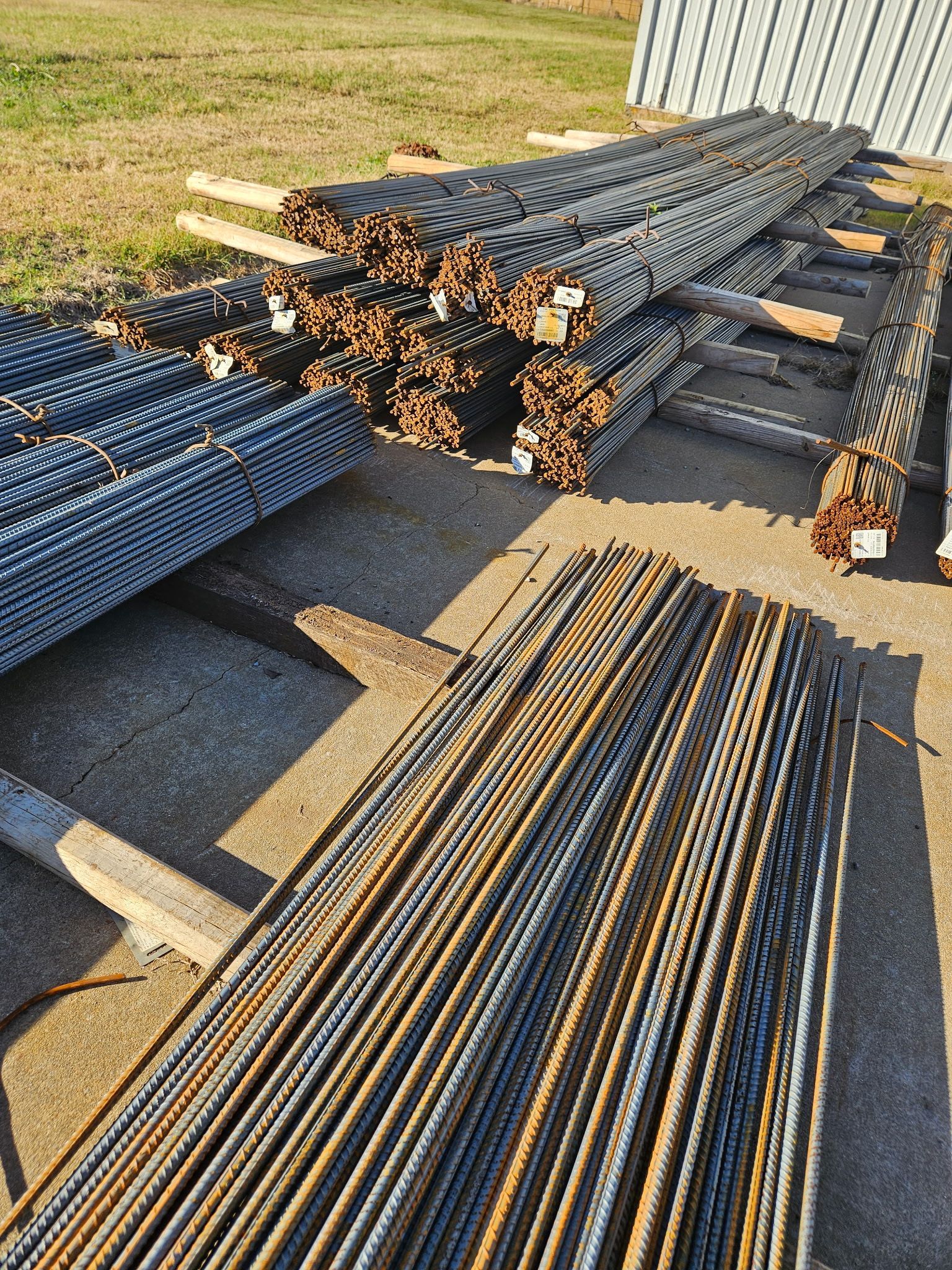 Piles of steel reinforcing bars (rebar) on wooden supports outdoors.