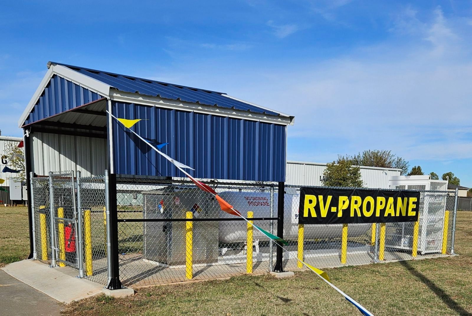 RV propane filling station with blue shelter and yellow sign against a blue sky.