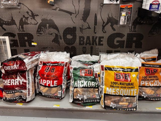 Bags of wood chips for grilling: cherry, apple, hickory, mesquite, and pecan, on a store shelf.