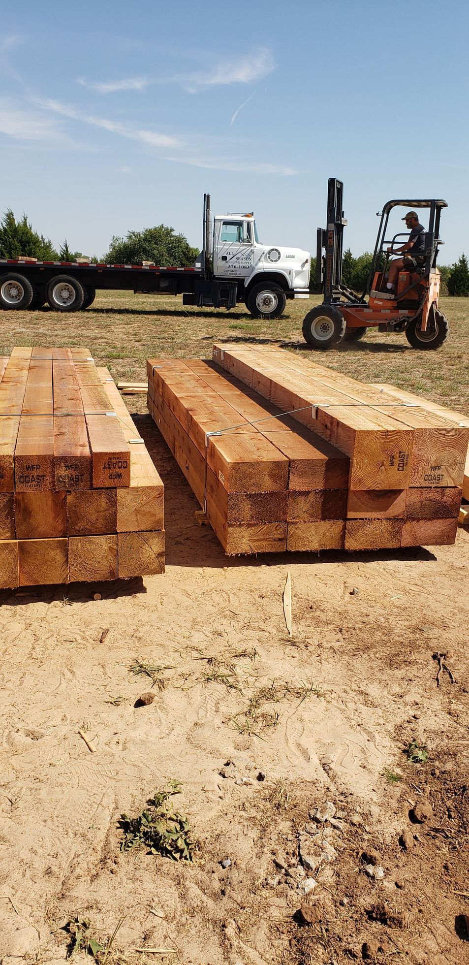 A truck and forklift loading lumber on a sunny day.