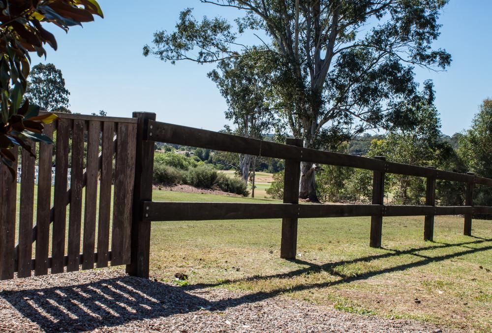 a Wooden Fence Surrounds a Grassy Field With Trees in the Background — Tony Sinclair Fencing In Bucca, NSW