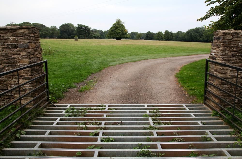 a Metal Gate Leading to a Dirt Road in a Field — Tony Sinclair Fencing In Coffs Harbour, NSW