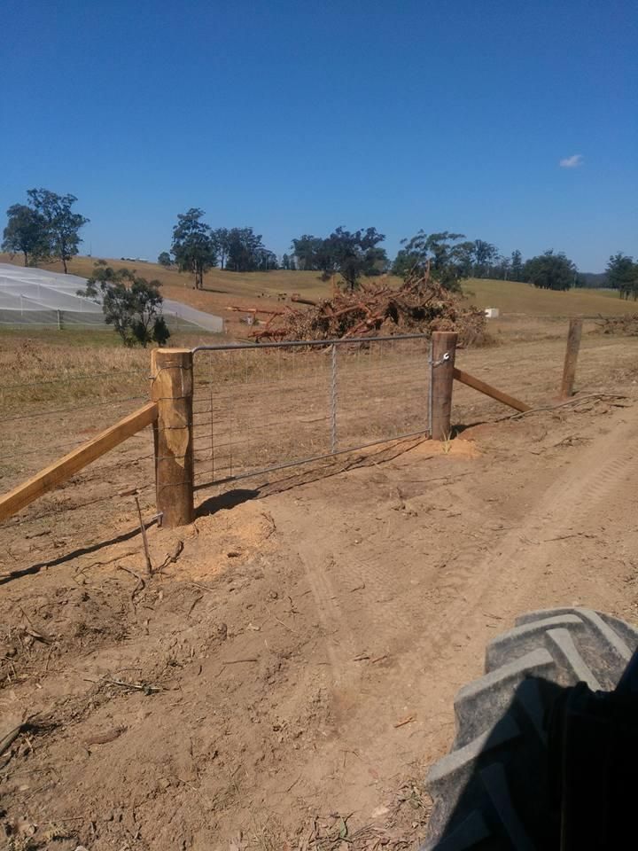 a Tractor is Driving Down a Dirt Road Next to a Wooden Fence — Tony Sinclair Fencing In Bucca, NSW
